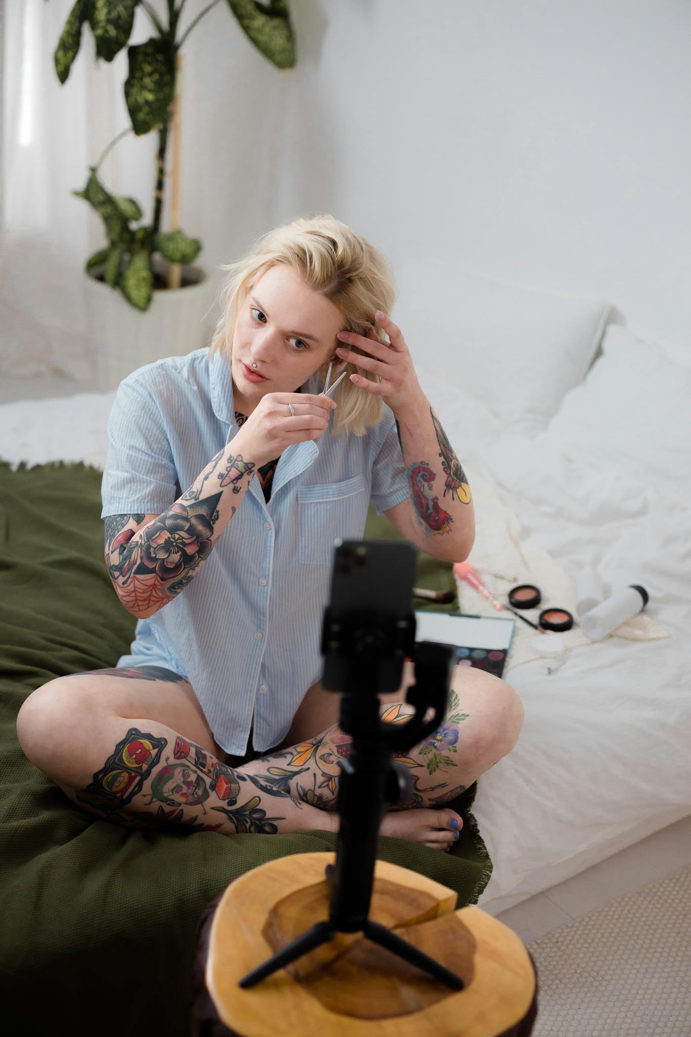 Tattooed woman creating video content at home, using a phone tripod.