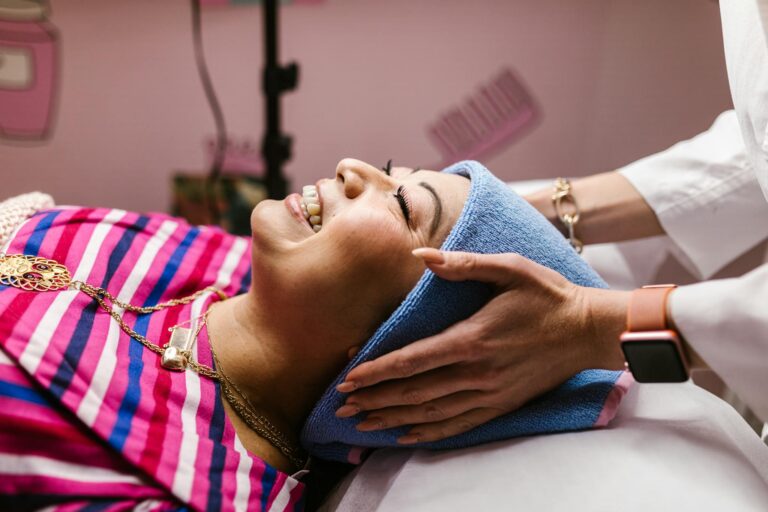 Woman enjoying a soothing facial massage at a spa with a warm smile, wrapped in a towel.